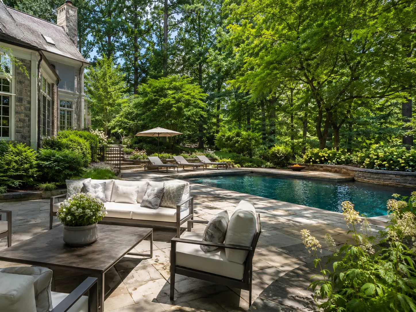 Luxury backyard in New Hope PA with pool, stone patio, outdoor seating, and wooded landscaping